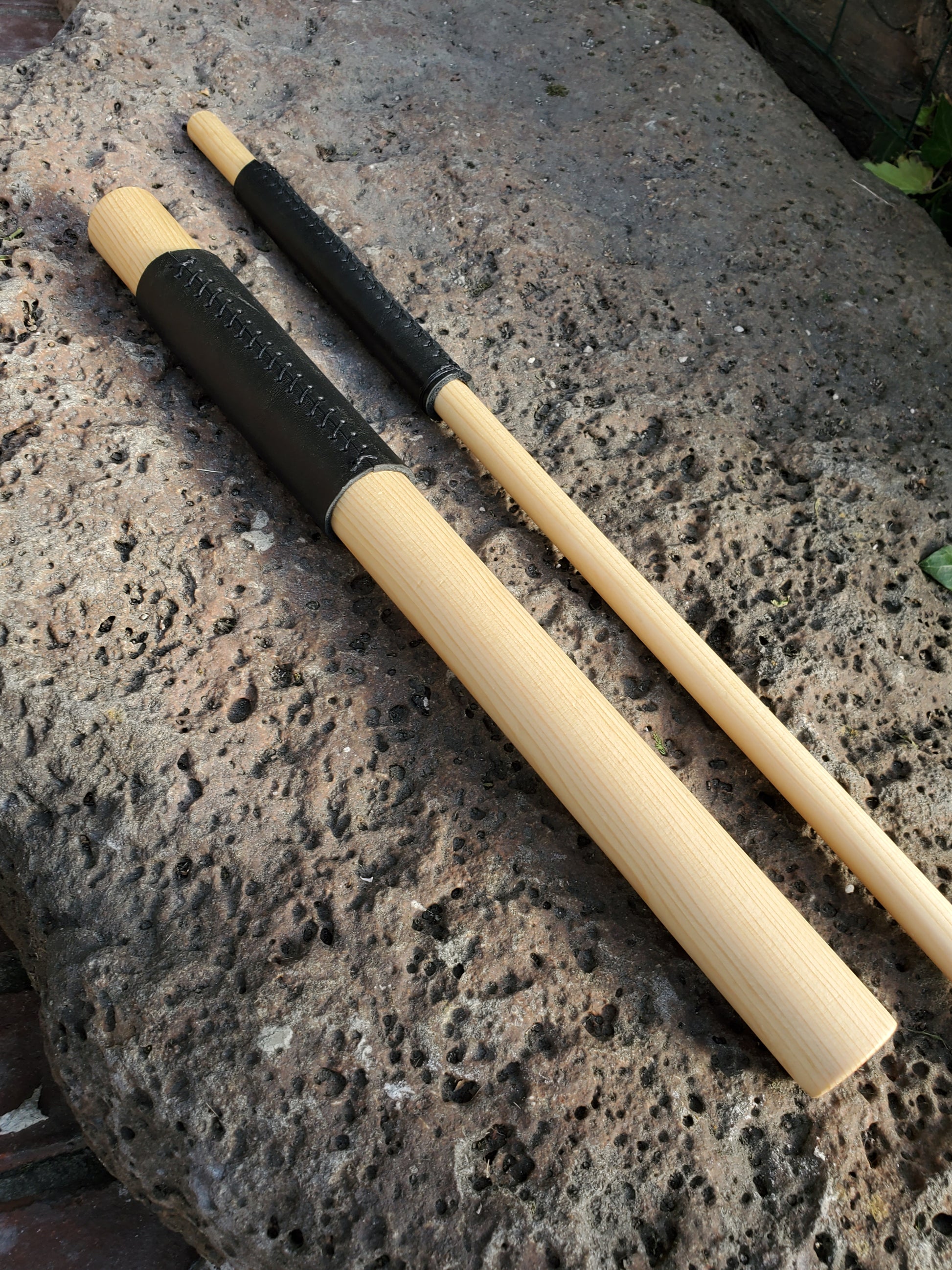 Two wooden sticks with black handles on a textured stone surface
