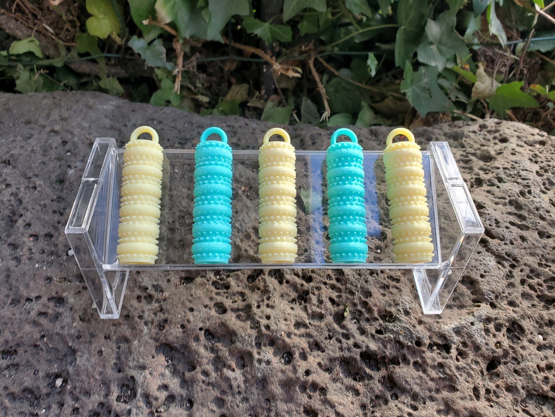 Five colorful cylindrical objects on a clear stand against a natural background
