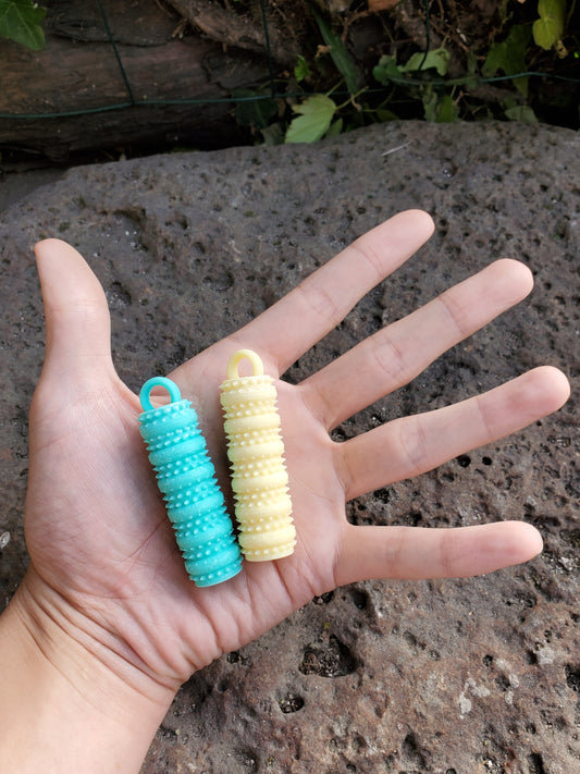 Hand holding two textured rings, one yellow and one blue, against a stone background.